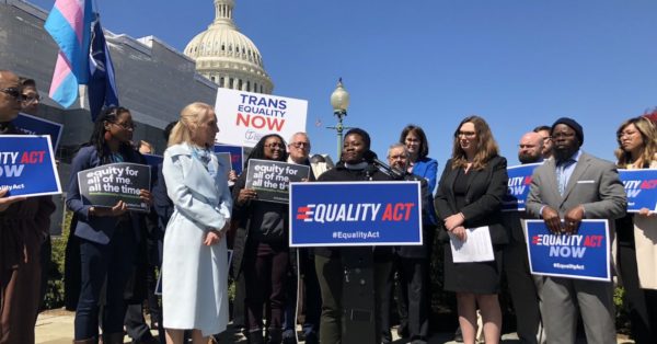 A press conference for the Equality Act outside the U.S. Capitol. People hold signs saying "Equality Act Now," "Trans Equality Now," and "Equity for all of me, all the time."