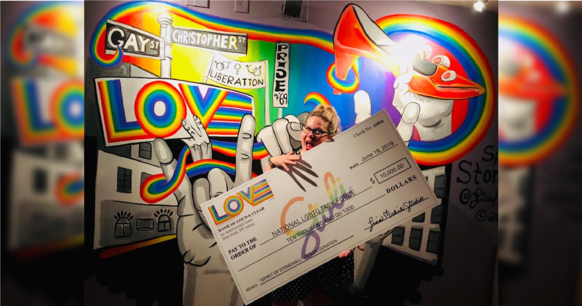 A person stands in front of a Stonewall mural holding a giant $10,000 check made out to the National LGBTQ Task Force.