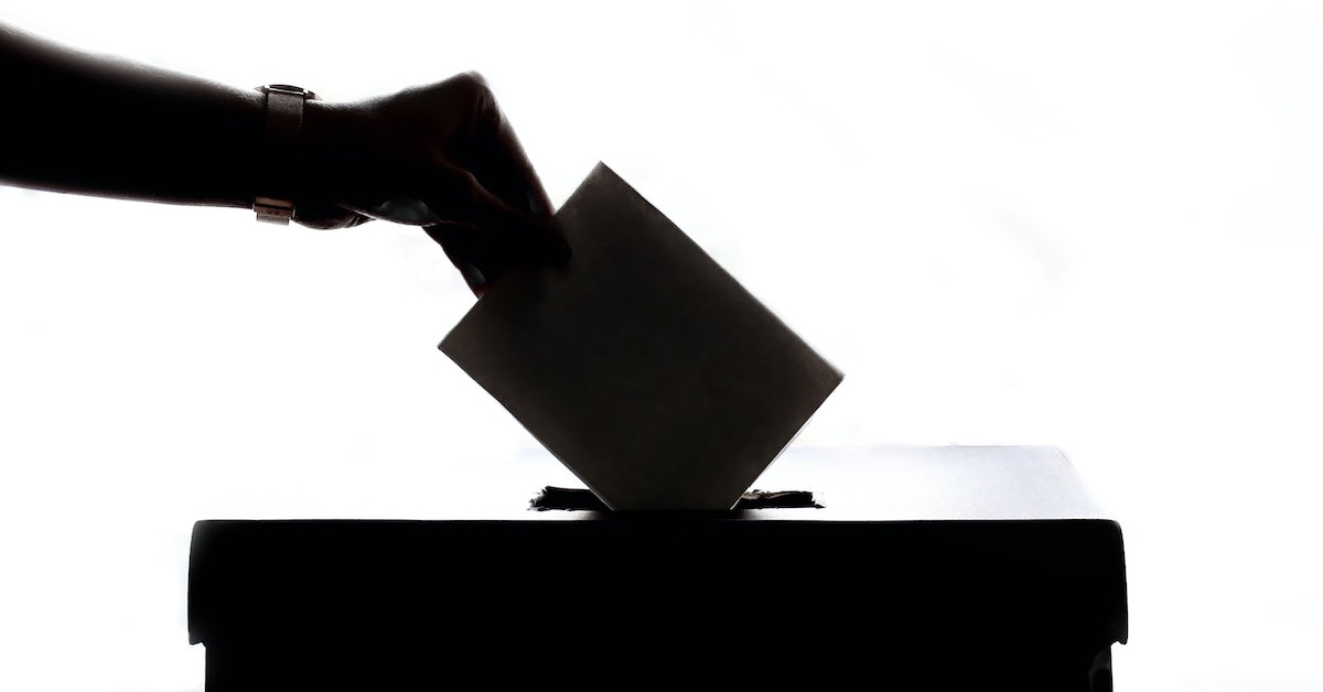 A hand putting a piece of paper into a ballot box.