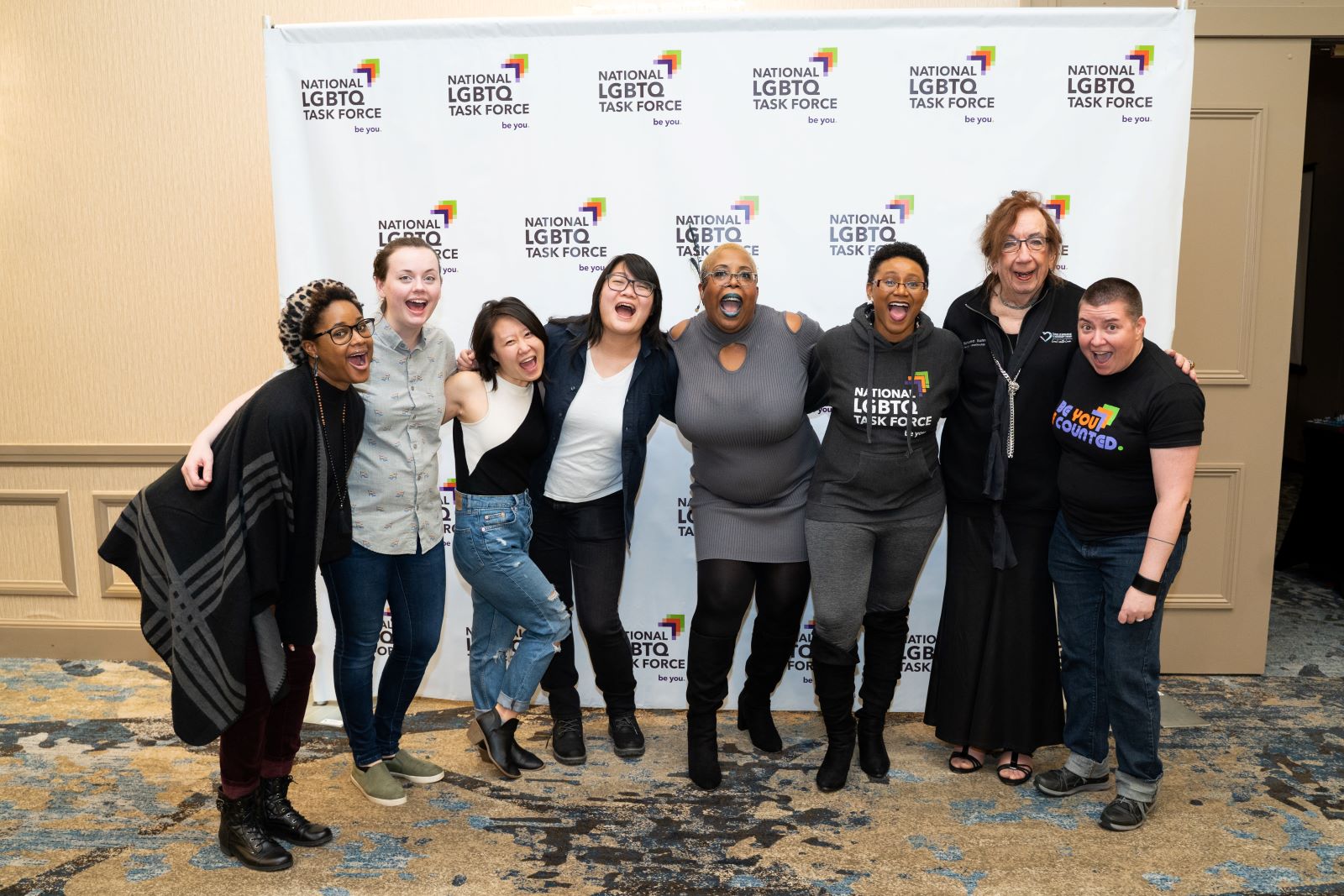 A group of multi-racial and multi-generation people pose happily in front of a large National LGBTQ Task Force background