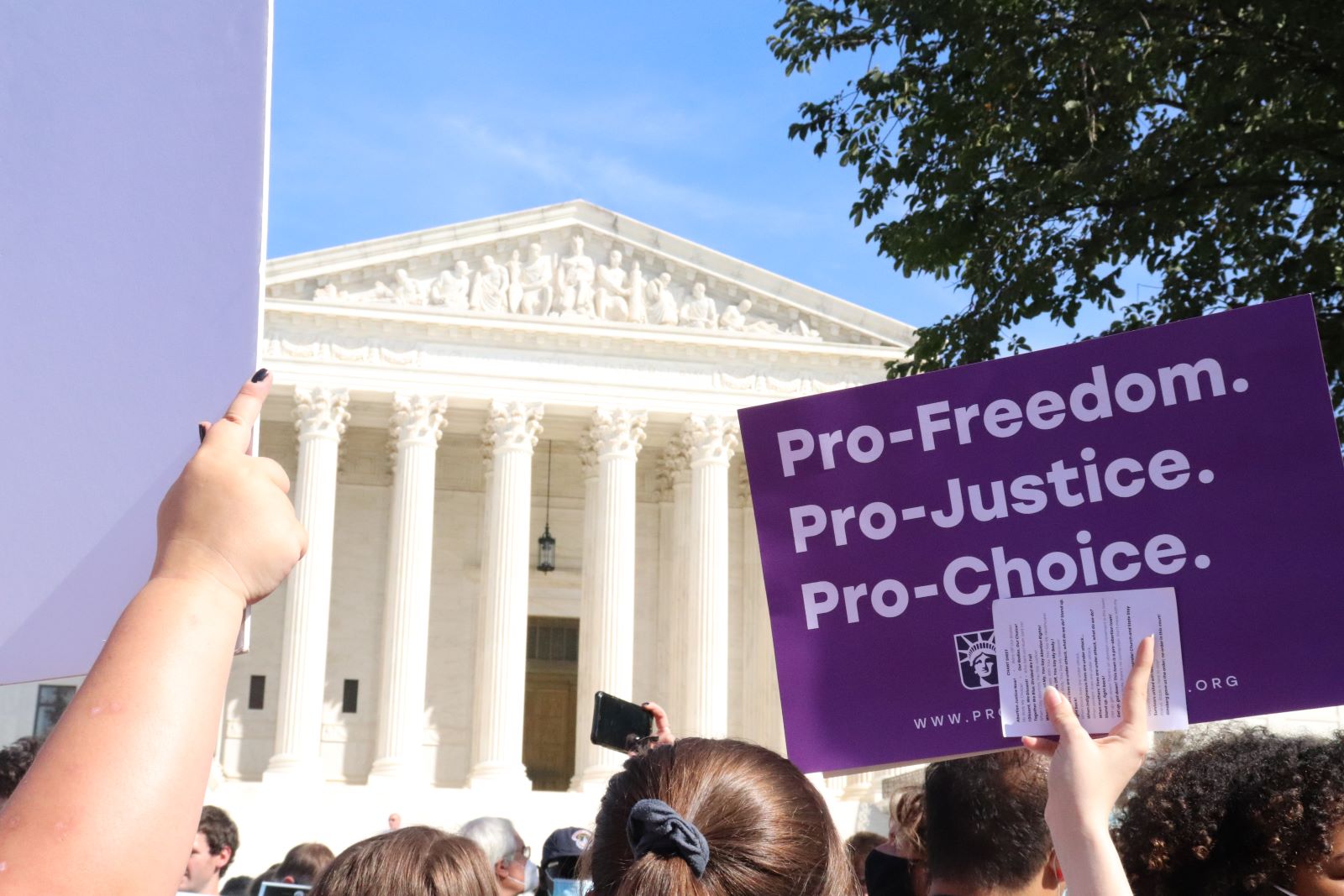 Una multitud se reúne frente a la Corte Suprema para una manifestación a favor del aborto. Detrás de la multitud, un letrero morado dice "Pro-Freedom. Pro-Justice. Pro-Choice".