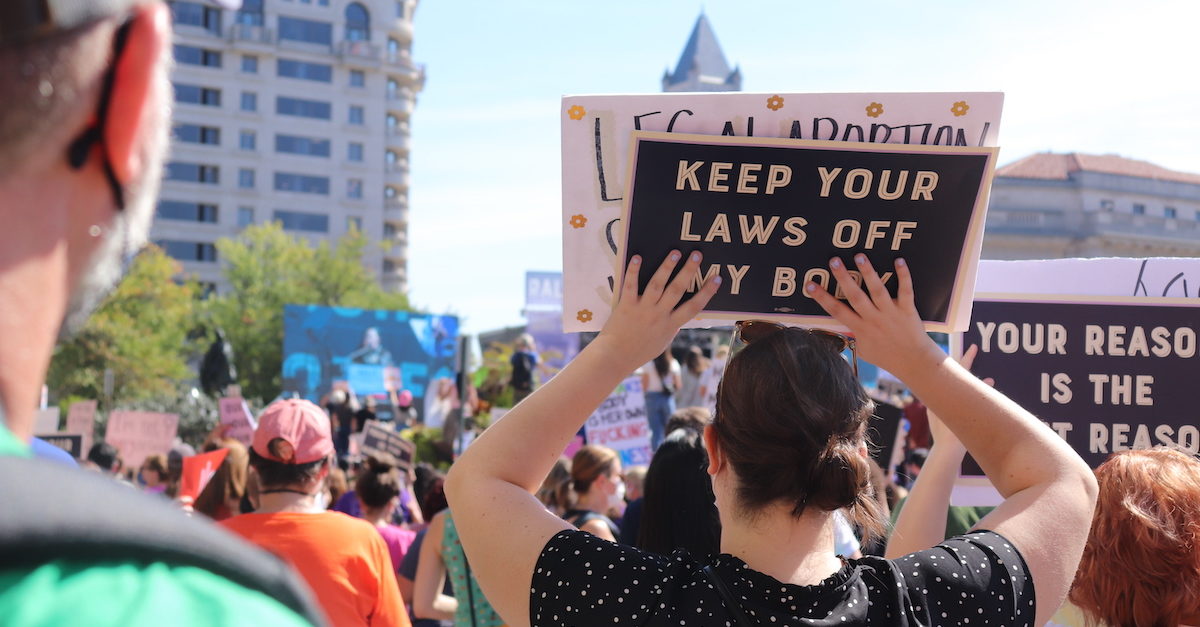 A large group of people gathered at a rally. In the foreground someone is holding a protest sign that says "Keep your laws off my body".