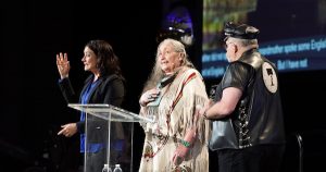 Three people stand on a stage as the Leather Leadership Award is given at the Creating Change Conference.