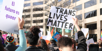 Un mitin con manifestantes con carteles que dicen "El futuro es queer" y "las vidas trans importan".