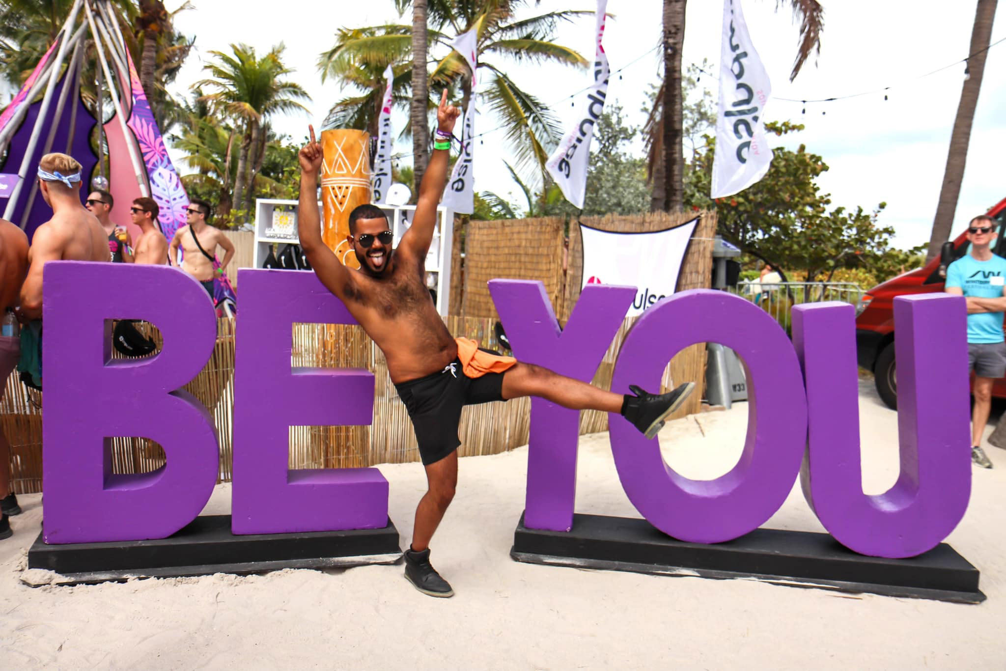 A person with both hands in the air, kicking one leg up, in front of large purple letters spelling out "BE YOU".