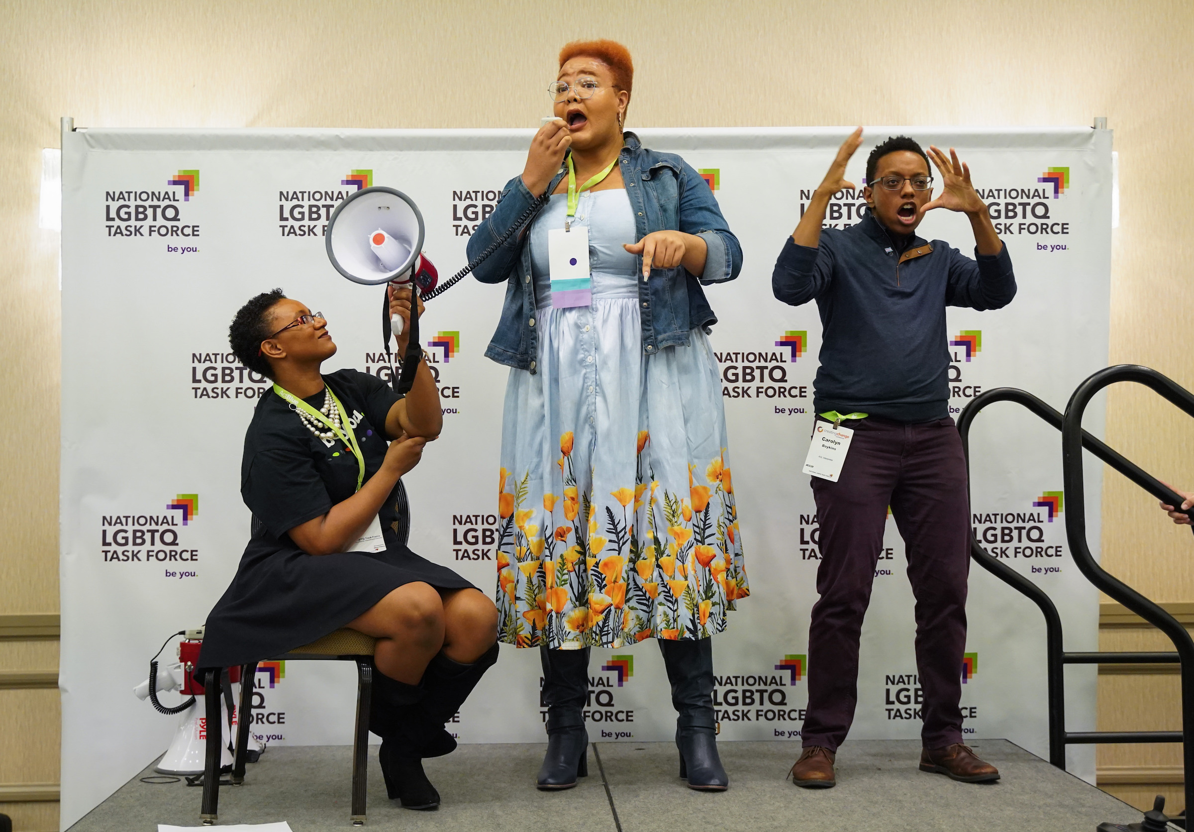 Viktoria Kirby York holds megaphone for Diamond (Stylz) Collier, Black Transwomen Inc Executive Director while black masc of center ASL interpreter signs at a rally