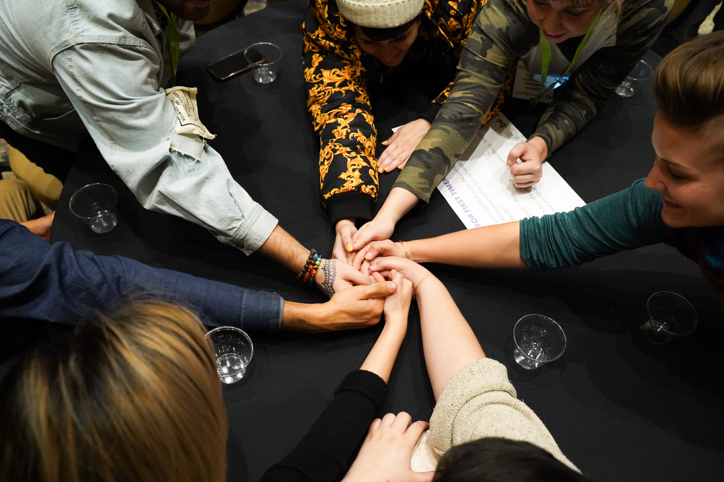 Multiracial group of people reaching into the center of a table to grasp hands