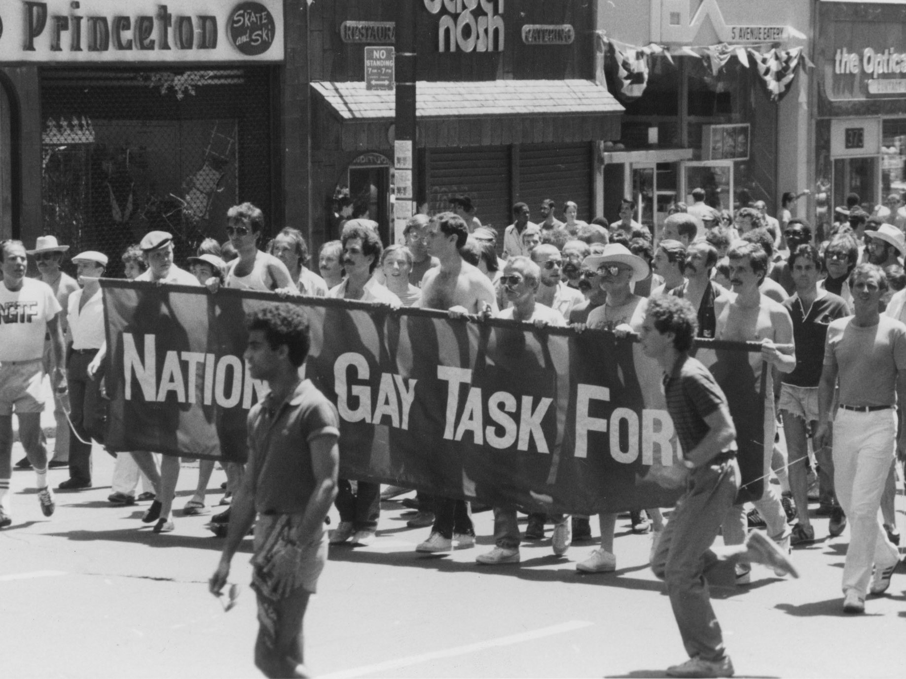 A black and white photo of people marching in the street behind a National Gay Task Force banner.