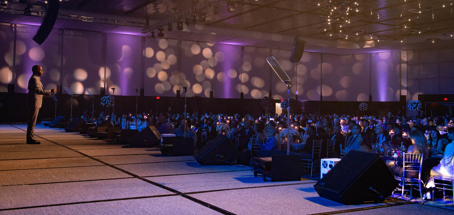 Image from the National LGBTQ Task Force's October 2022 Gala. Photo show a dimly lit ballroom full of hundreds of guests seated at their round tables and Jonathan Capehart speaking on the stage.