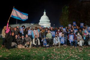 Un grupo de personas frente al Capitolio de Estados Unidos con carteles que dicen "Las personas trans pertenecen". Están sonriendo y mirando a la cámara.