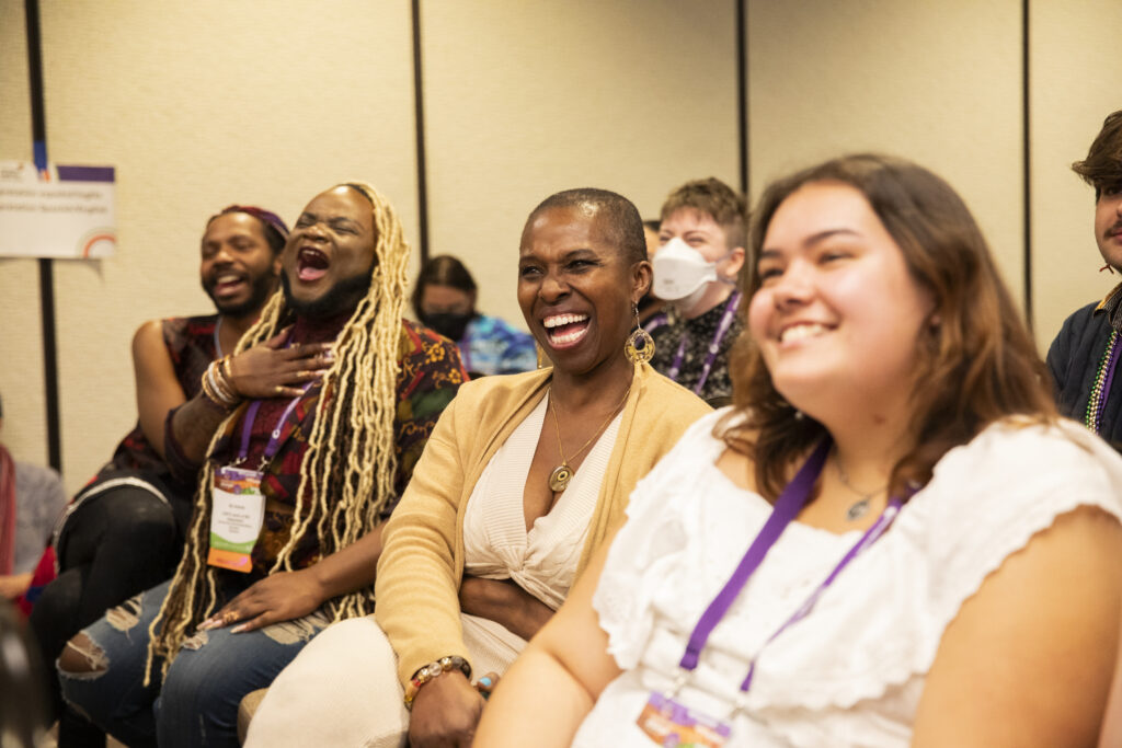 A group of audience members smiling and laughing in a conference room at a panel session.