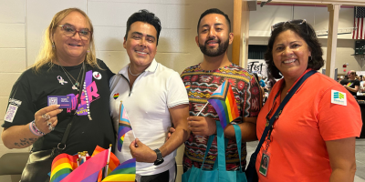 Four people pose holding rainbow flags at Pride