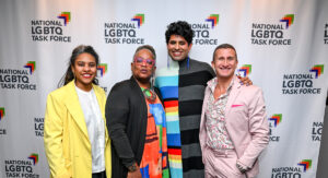 People in colorful clothes standing in front of a LGTBQ banner